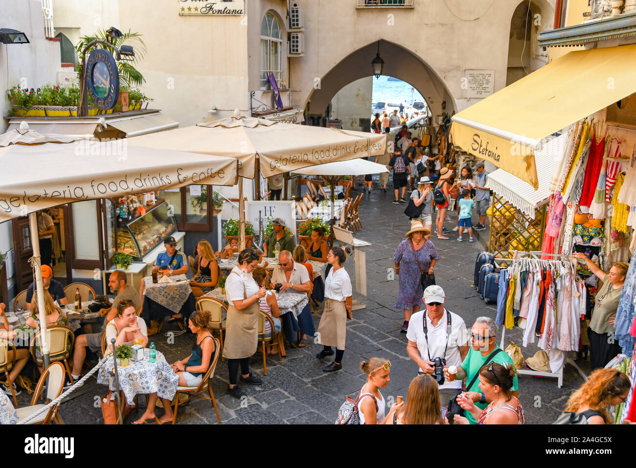 AMALFI, ITALIEN - AUGUST 2019: Leute an den Tischen draußen ein Restaurant und Geschäfte im Zentrum von Amalfi. Stockfoto