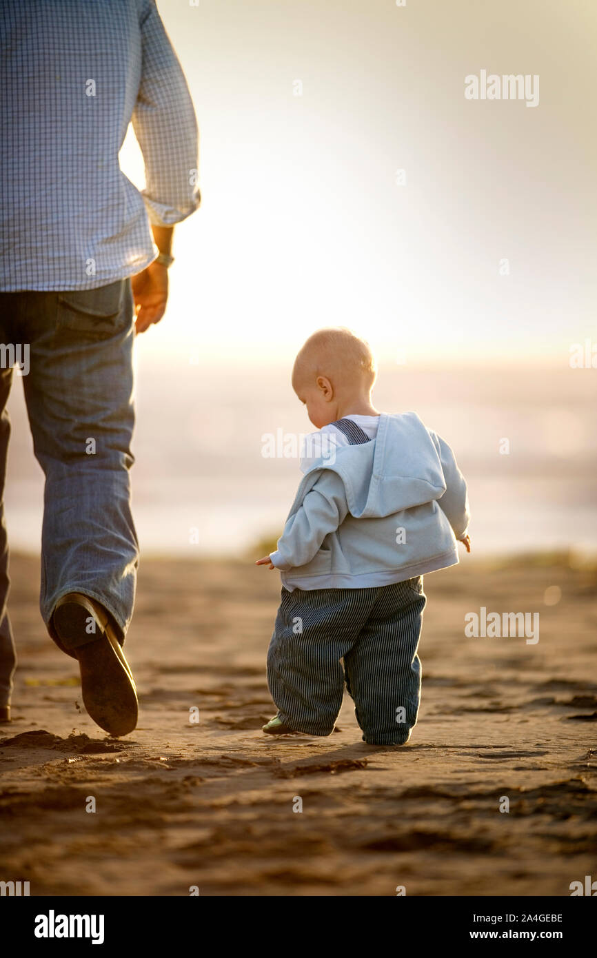 Kleinkind zu Fuß neben seinem Vater auf dem Strand. Stockfoto