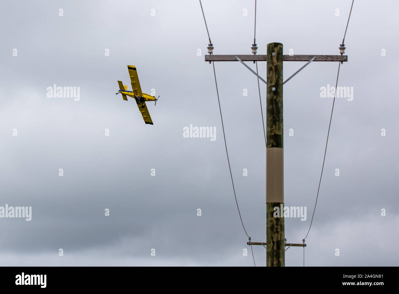 Sheffield, Canterbury, Neuseeland, 14. Oktober 2019: Ein gelbes Crop duster, oder Top dressing Flugzeug, niedrige über Stromleitungen als es breitet sich aus, Dünger Stockfoto