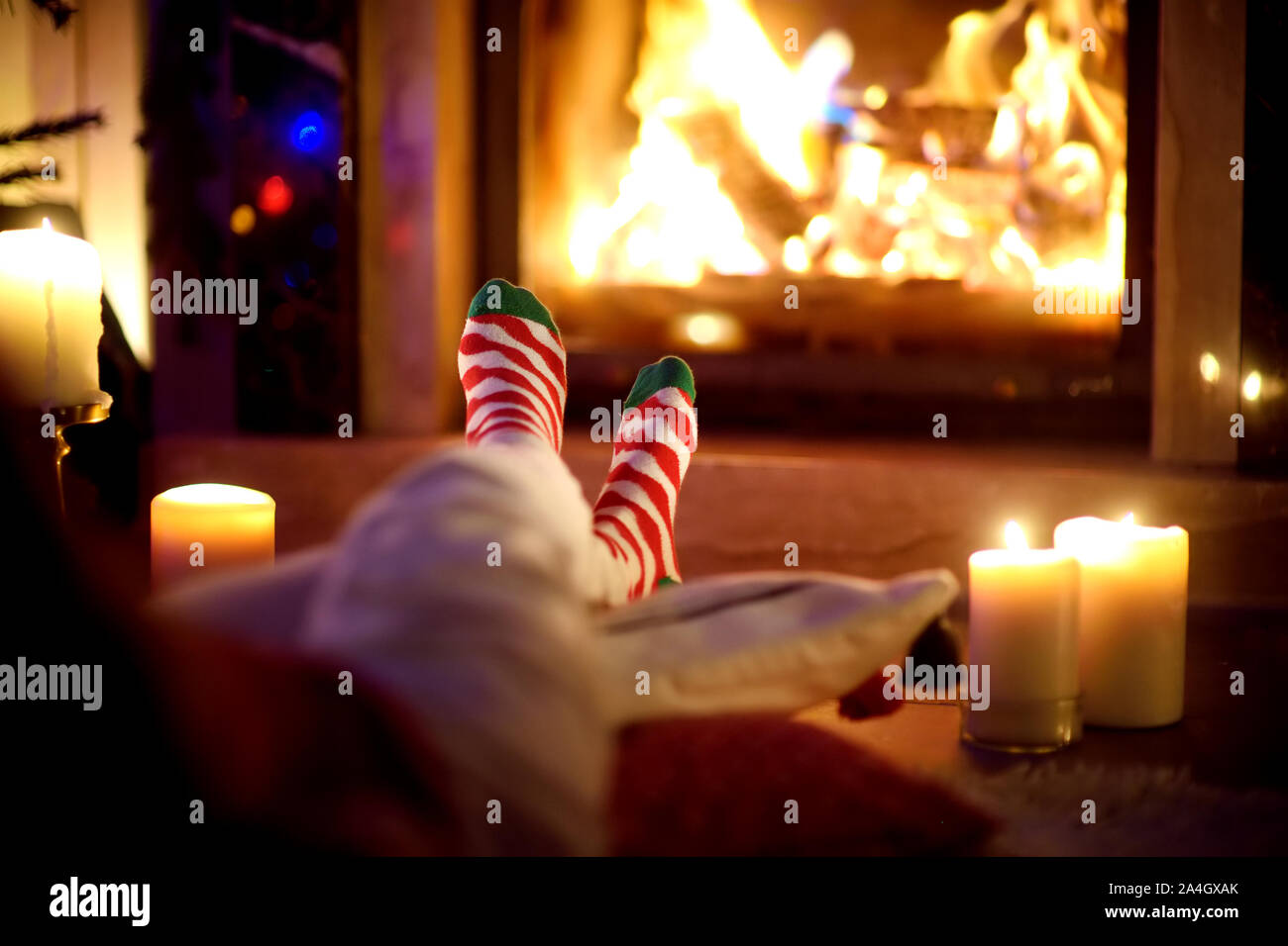 Frau ruht Ihre Beine in gestreiften festliche Socken in ein Zimmer mit Kamin und Kerzen auf gemütlichen Weihnachtsabend. Happy festliche Zeit im Winter Stockfoto