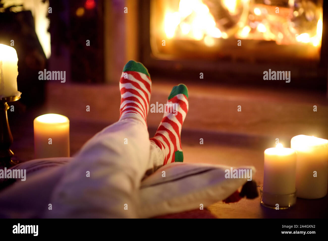 Frau ruht Ihre Beine in gestreiften festliche Socken in ein Zimmer mit Kamin und Kerzen auf gemütlichen Weihnachtsabend. Happy festliche Zeit im Winter Stockfoto