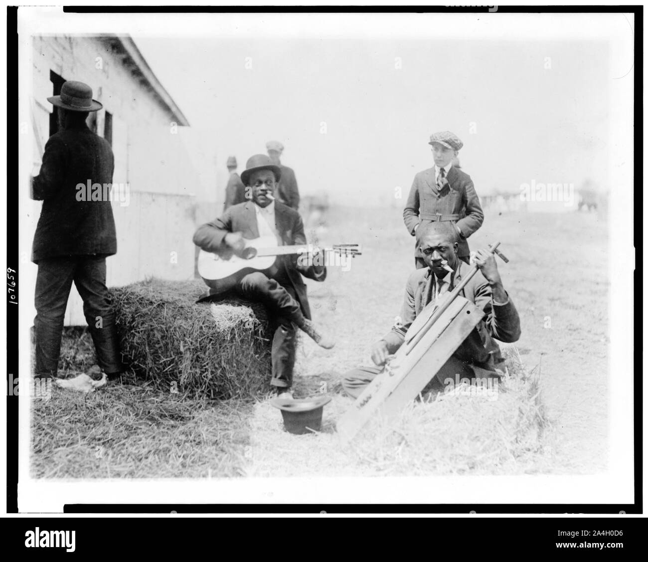 Zwei afro-amerikanische Männer, außerhalb von stabilen, mit Kazoos in ihren Mund, einer von Ihnen sitzt auf haybale und Gitarre gespielt, die anderen Spielen hausgemachte Saiteninstrument, Washington, D.C. oder New York City Stockfoto