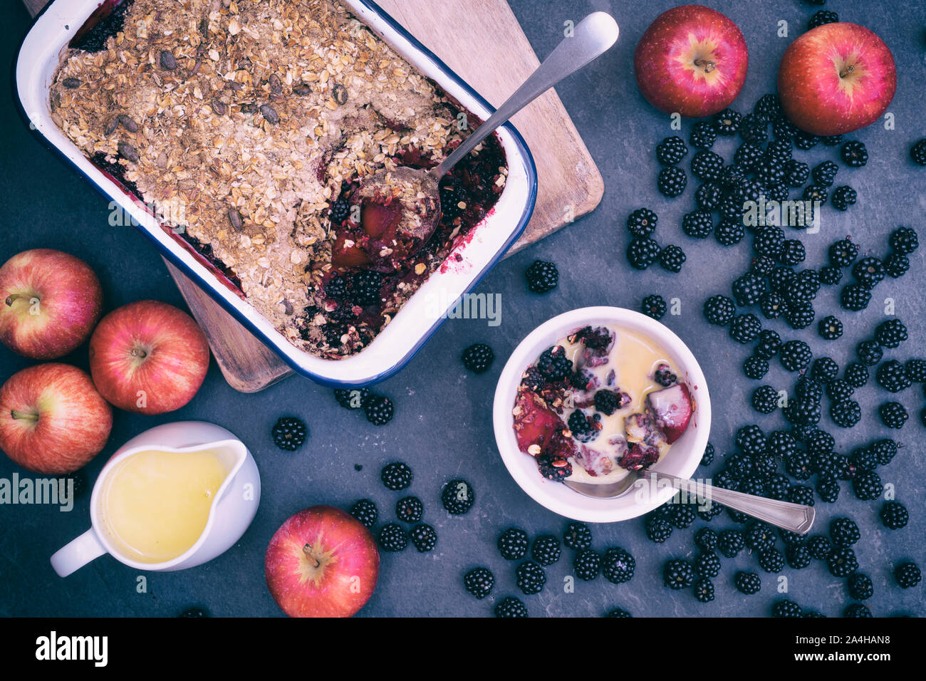 Hausgemachte Black und Apple Crumble und Vanillepudding mit einem Eßlöffel. Bio Hafer und Samen mit hat Brombeeren und Äpfel bröckeln Stockfoto