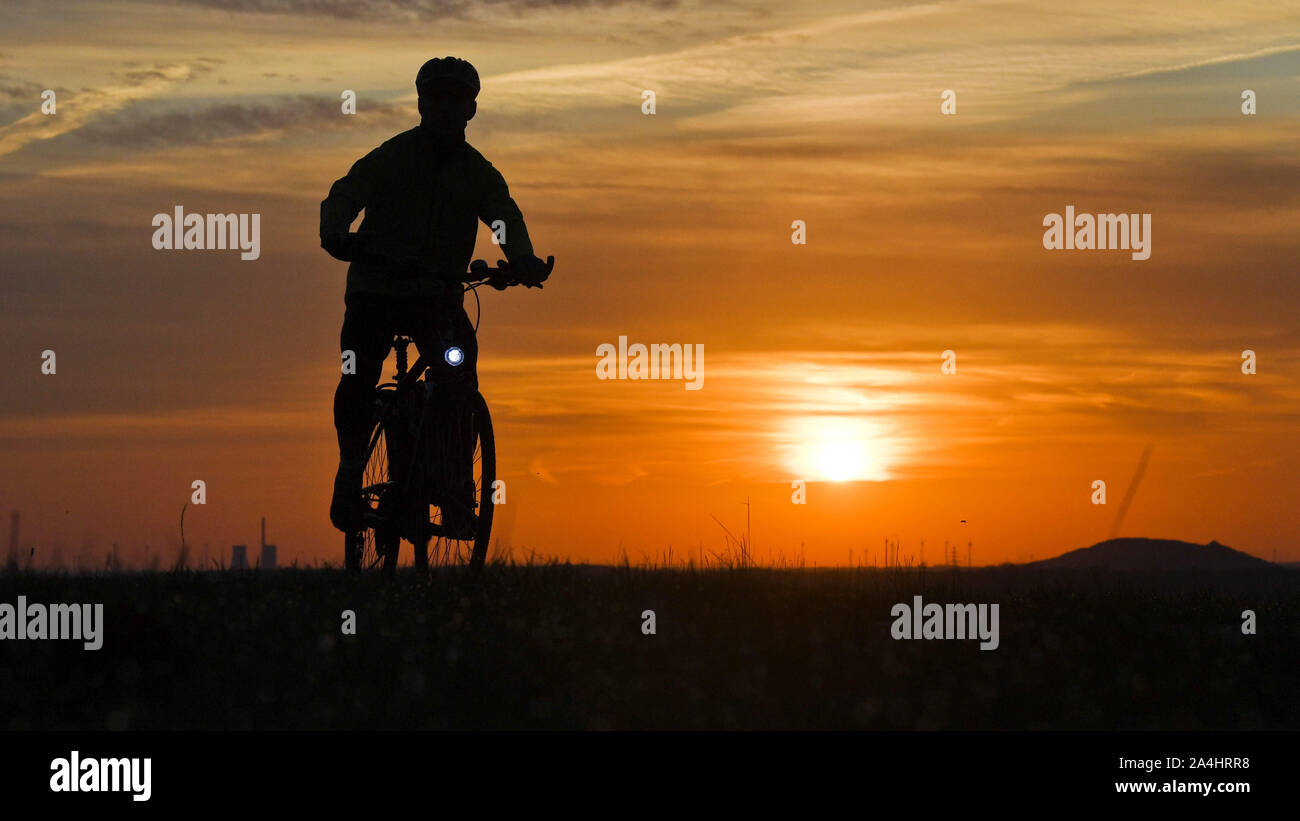 Hannover, Deutschland. 15 Okt, 2019. Ein Mann reitet ein Fahrrad entlang einem Feldweg kurz nach Sonnenaufgang. Credit: Julian Stratenschulte/dpa/Alamy leben Nachrichten Stockfoto
