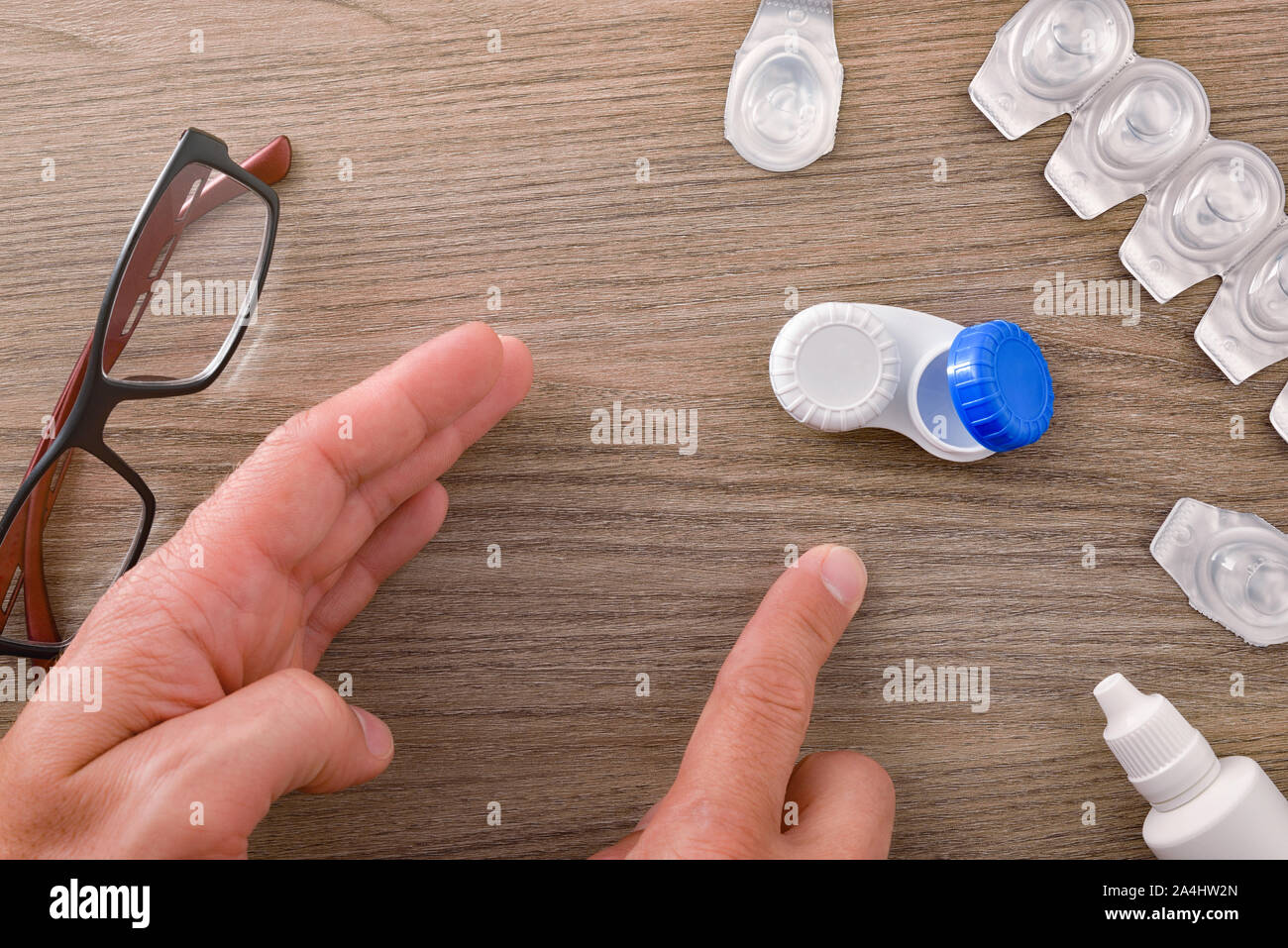 Die Hände eines Mannes auf die Präferenz der Kontaktlinsen statt Brille auf einem Holztisch. Horizontale Komposition. Ansicht von oben. Stockfoto