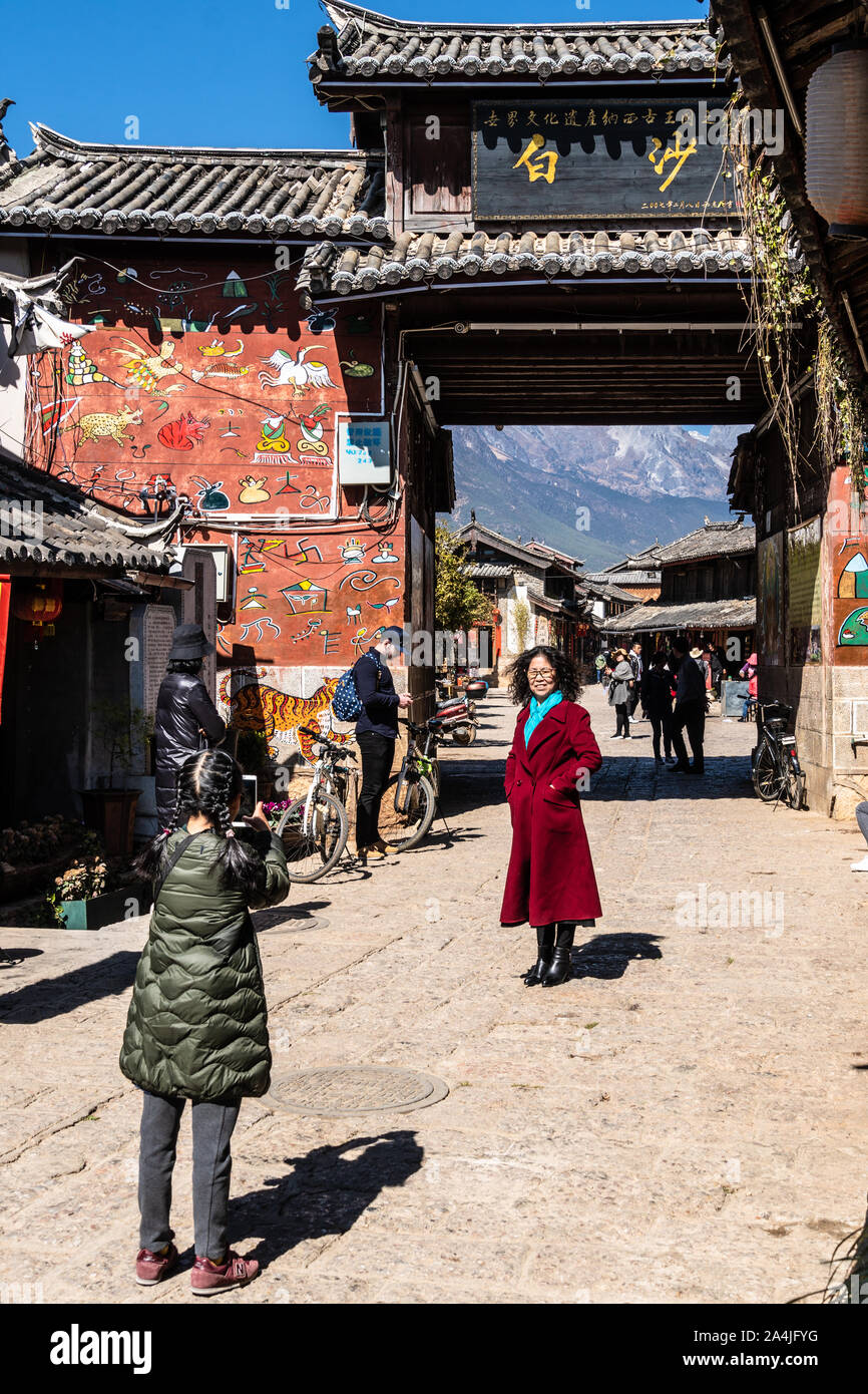 Baisha, China - 11. Februar 2019: Chinesische weibliche Touristen posieren für ein Foto vor dem traditionellen Bai Sha Naxi Dorf Eingangstor in der Nähe von Lijian Stockfoto