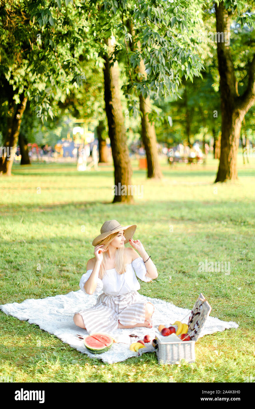 Junge aucasian Mädchen in der Hut sitzt im Garten auf Plaid in der Nähe von Früchten, Bäume im Hintergrund. Stockfoto