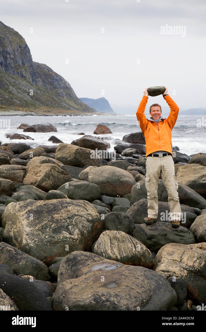 Starke Mann in orange Jacke, Alnes bei Godoy - Anheben von schweren Stein Stockfoto