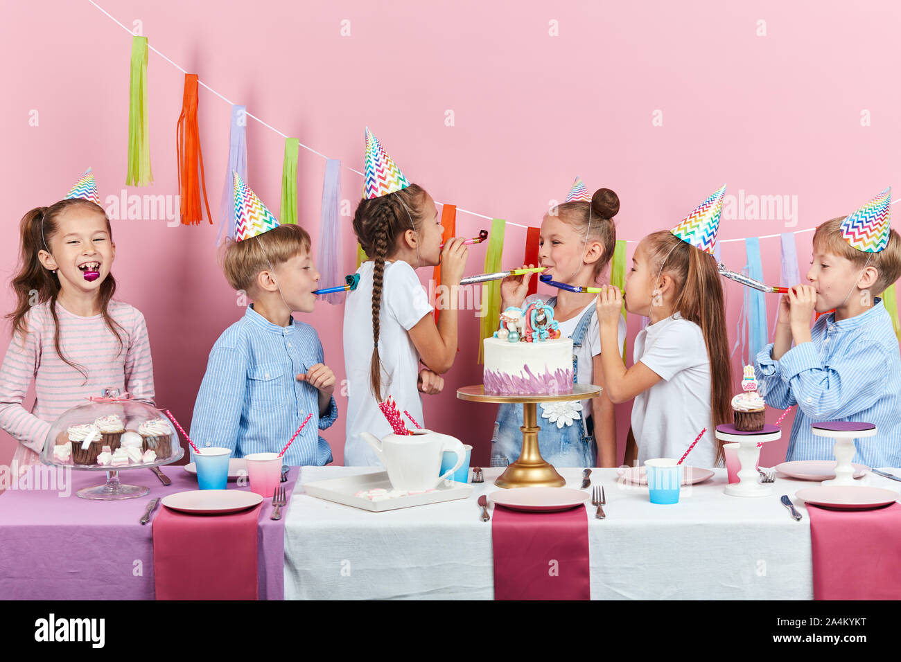 Lustige kleine Jungen und Mädchen blasen in die Partei Hörner, unterhaltsam, isolierte rosa Hintergrund, Urlaub, festliche Zeit Stockfoto