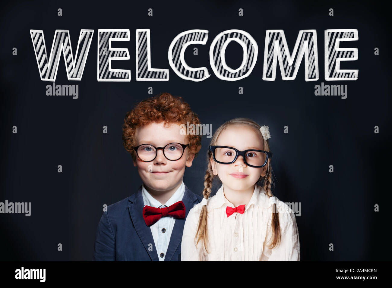 Student Kinder Jungen und Mädchen gegen Schiefertafel Hintergrund mit Willkommen Inschrift Stockfoto