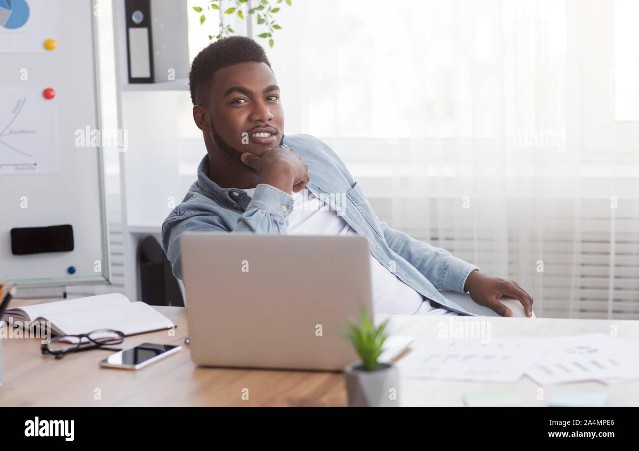 Junge schwarze Unternehmer am Arbeitsplatz sitzen in seinem eigenen Büro. Stockfoto