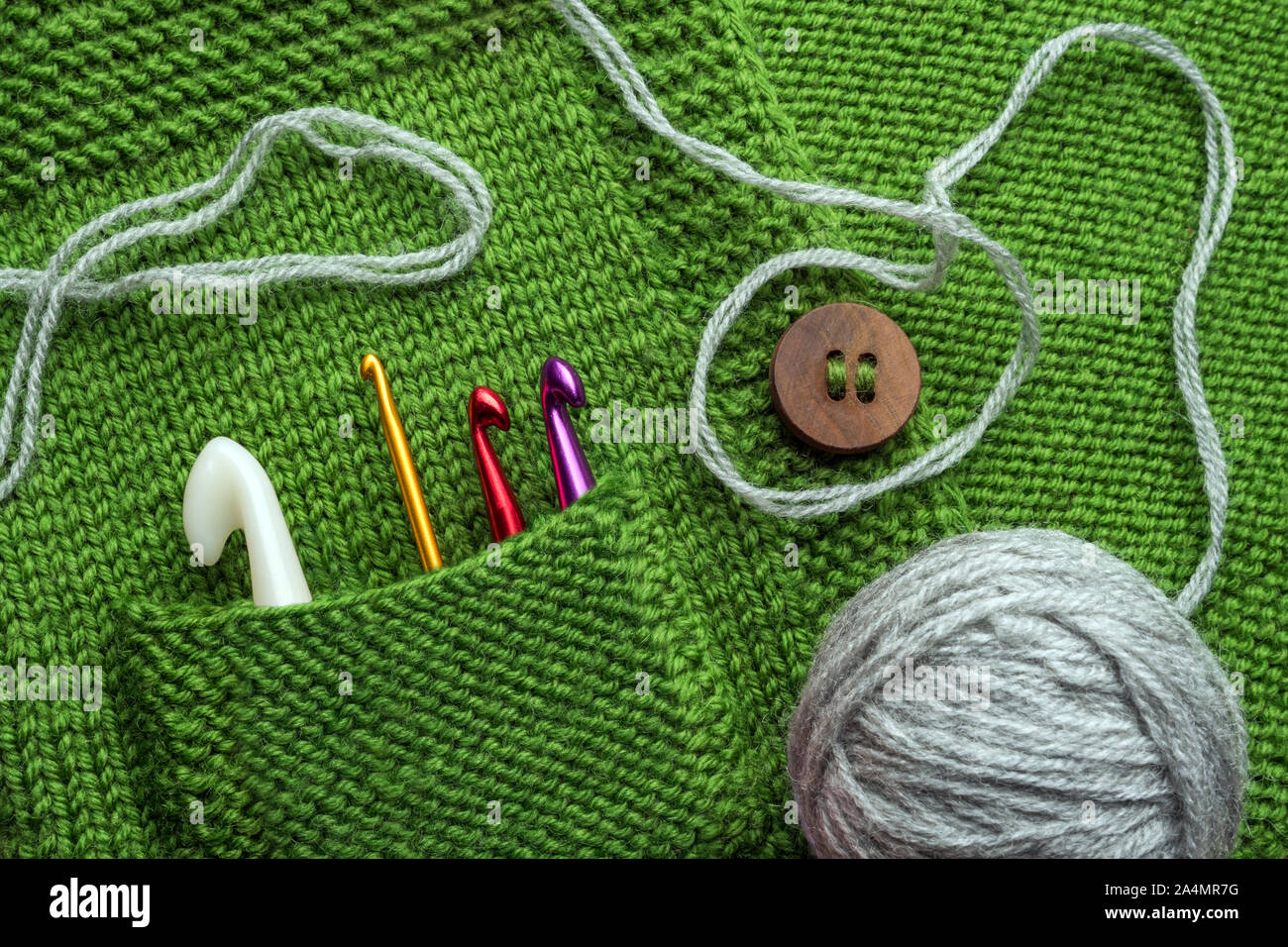 Gestaltete Konzept. Handgefertigte Hintergrund. Häkelnadeln in grün Tasche. Fragment der Handgefertigte Kleidung mit Haken in der Tasche. Holz- Tasten auf handgemachte Pullover. Stilvolle Kleidung gestalteten, handgefertigten Stockfoto