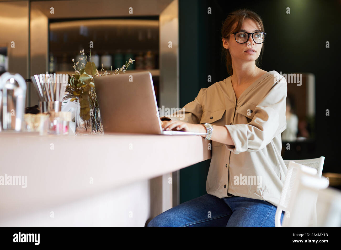 Ernsthafte junge Frau in eyelasses und in Freizeitkleidung Tippen auf Laptop während der Sitzung in Cafe Stockfoto