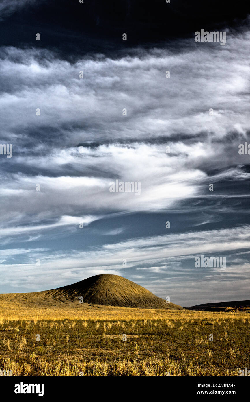 Ein einsamer Hügel im Grasland mit weißen Puffy clouds Overhead. Stockfoto