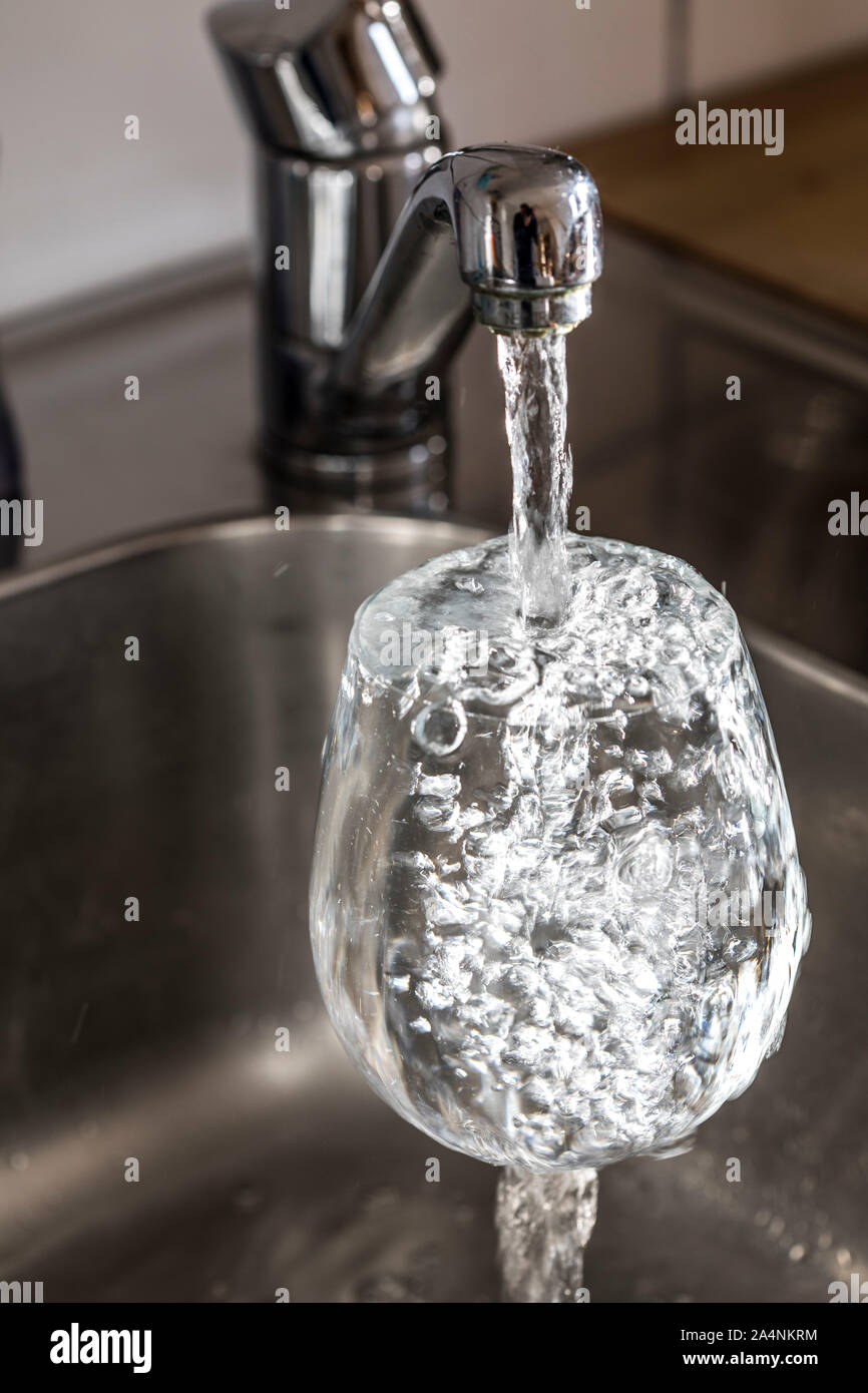 Fließt das Wasser aus einem Hahn in ein Glas. Symbol: Wasserverbrauch, Verschwendung von Wasser. Stockfoto