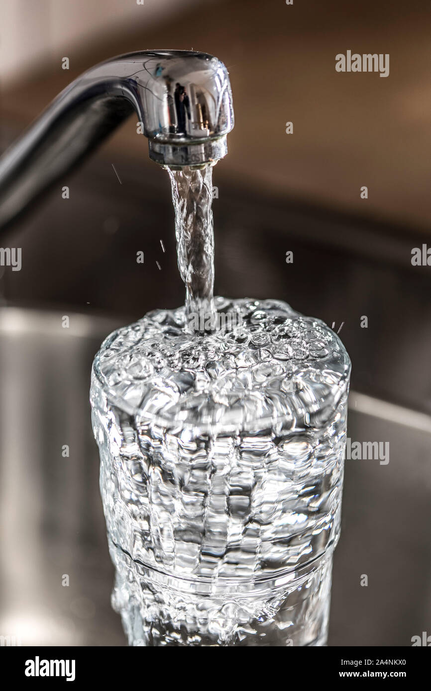 Fließt das Wasser aus einem Hahn in ein Glas. Symbol: Wasserverbrauch, Verschwendung von Wasser. Stockfoto