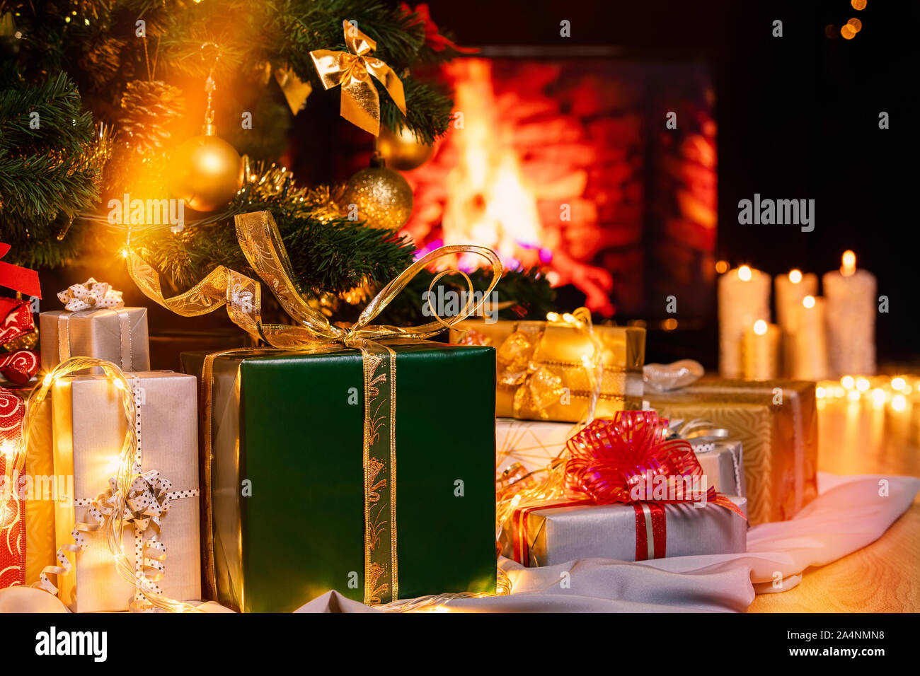 Stapel von verpackten Geschenksets unter dem Weihnachtsbaum mit brennenden Kamin. Viele Weihnachten Geschenke unter dem Baum. Kerzen auf Holzboden. Fokus auf g Stockfoto