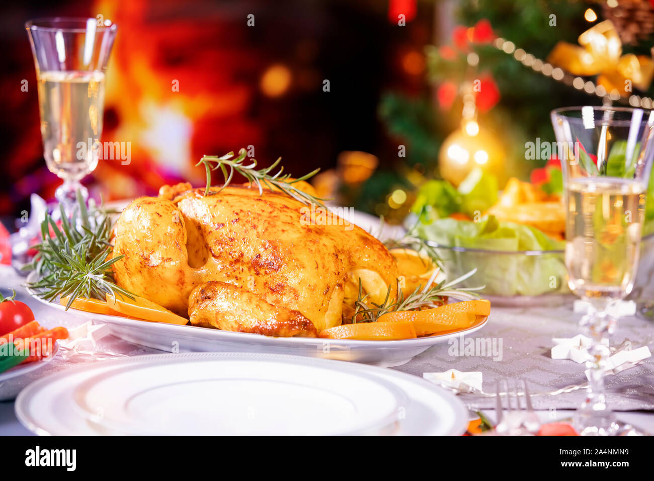 Weihnachtsessen. Huhn gegen glühende Weihnachtsbeleuchtung und brennenden Kerzen. Ferienwohnung gedeckter Tisch, Weihnachtsbaum, Champagner und gebratener Truthahn, Stockfoto