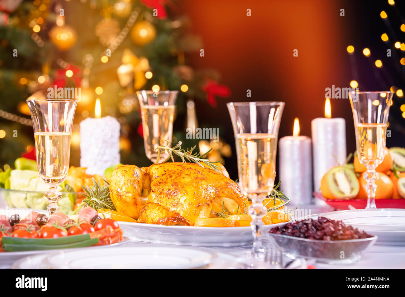 Weihnachtsessen. Huhn gegen glühende Weihnachtsbeleuchtung und brennenden Kerzen. Ferienwohnung gedeckter Tisch, Weihnachtsbaum, Champagner und gebratener Truthahn, Stockfoto