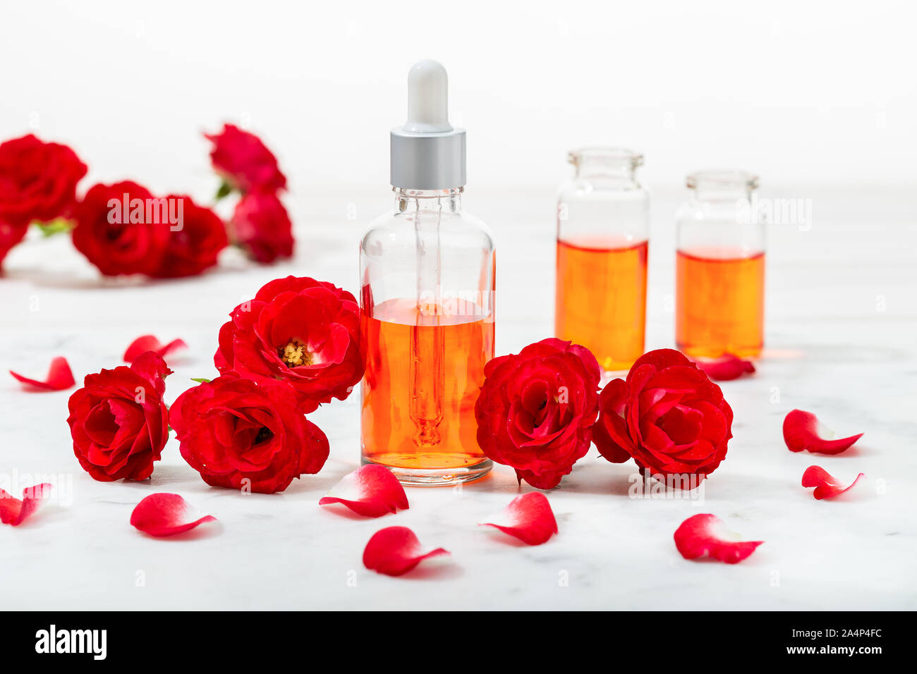 Duftende rose Wasser in Glasflaschen und kleine rote Rosen mit Blüten. Massage, Aromatherapie und Naturkosmetik Konzept Stockfoto