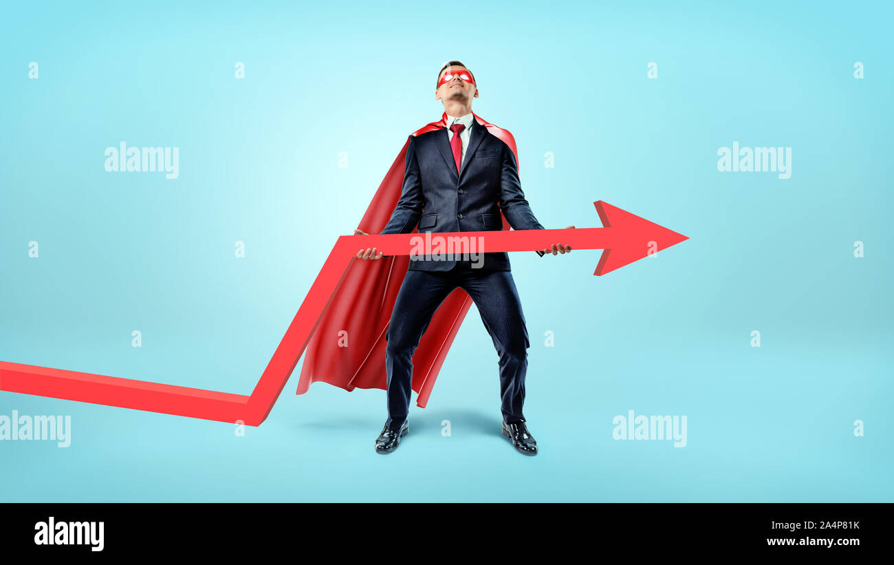Ein Geschäftsmann in einem roten fließende Kap versuchen, ein großer, roter Pfeil nach oben auf blauem Hintergrund zu heben. Stockfoto
