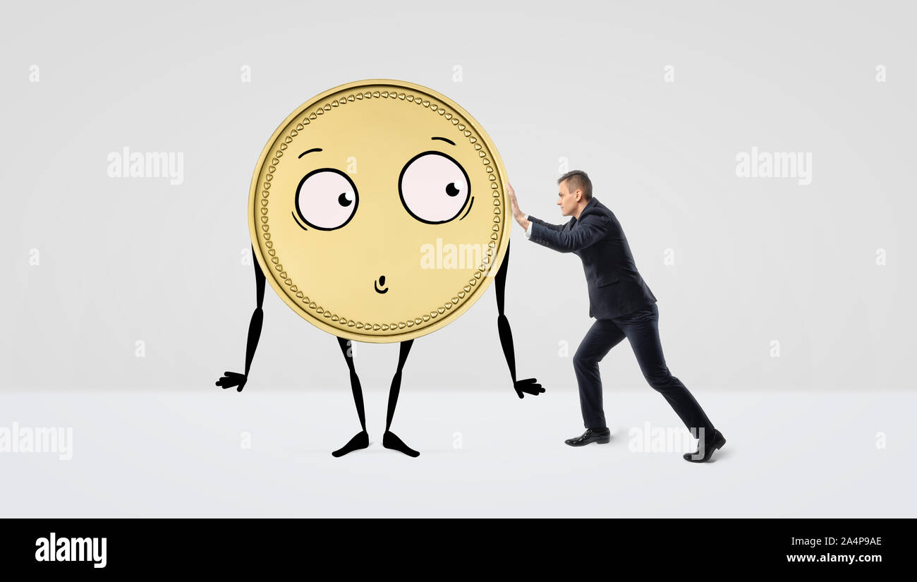 Ein Geschäftsmann versucht, eine goldene Münze mit Armen, Beinen und einem Gesicht, auf weißem Hintergrund zu schieben. Stockfoto