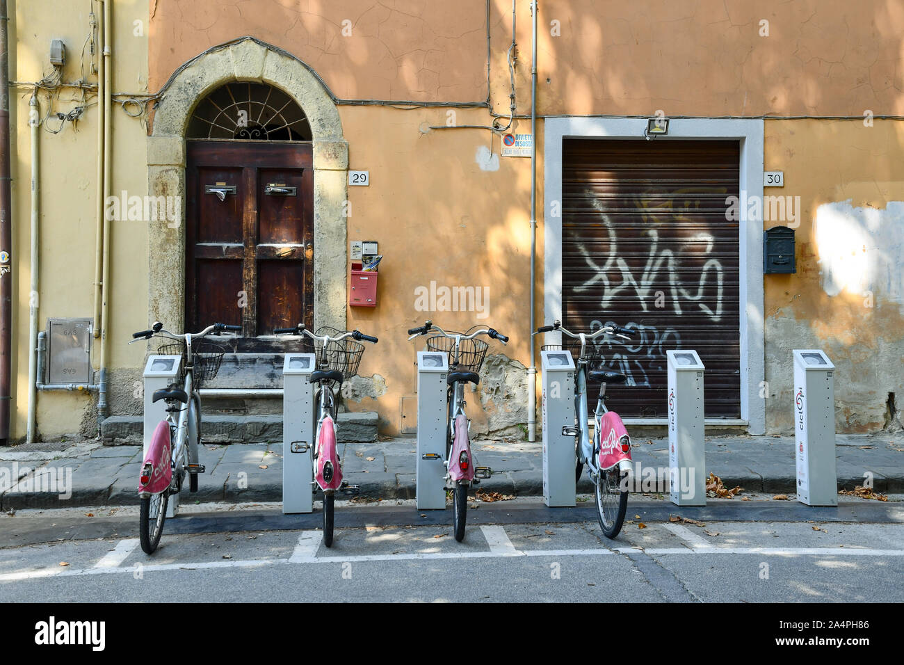 Zeile der öffentlichen Fahrräder, die zu einem Bike Sharing Station vor einem alten Gebäude im historischen Zentrum der berühmten Stadt Pisa, Toskana, Italien geparkt Stockfoto