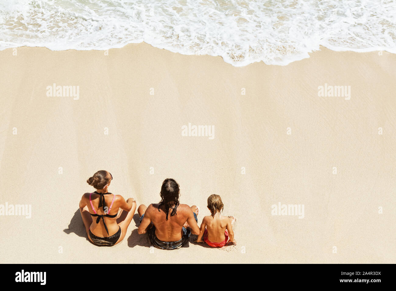 An sonnigen Strand glückliche Kinder mit Eltern Spaß haben, sitzen auf weißen Sand am Meer surfen mit Schaum und Spritzer zu sehen. Ansicht von oben. Aktive Kinder Sommer Lifestyle. Stockfoto