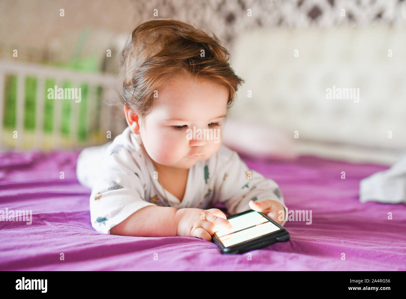 Kind sucht zu Telefonen. Strahlung vom Telefon auf das Kind. Ein kleiner Junge 0-1 Jahre alt mit einem Smartphone in seinen Händen sieht am Bildschirm mit Stockfoto