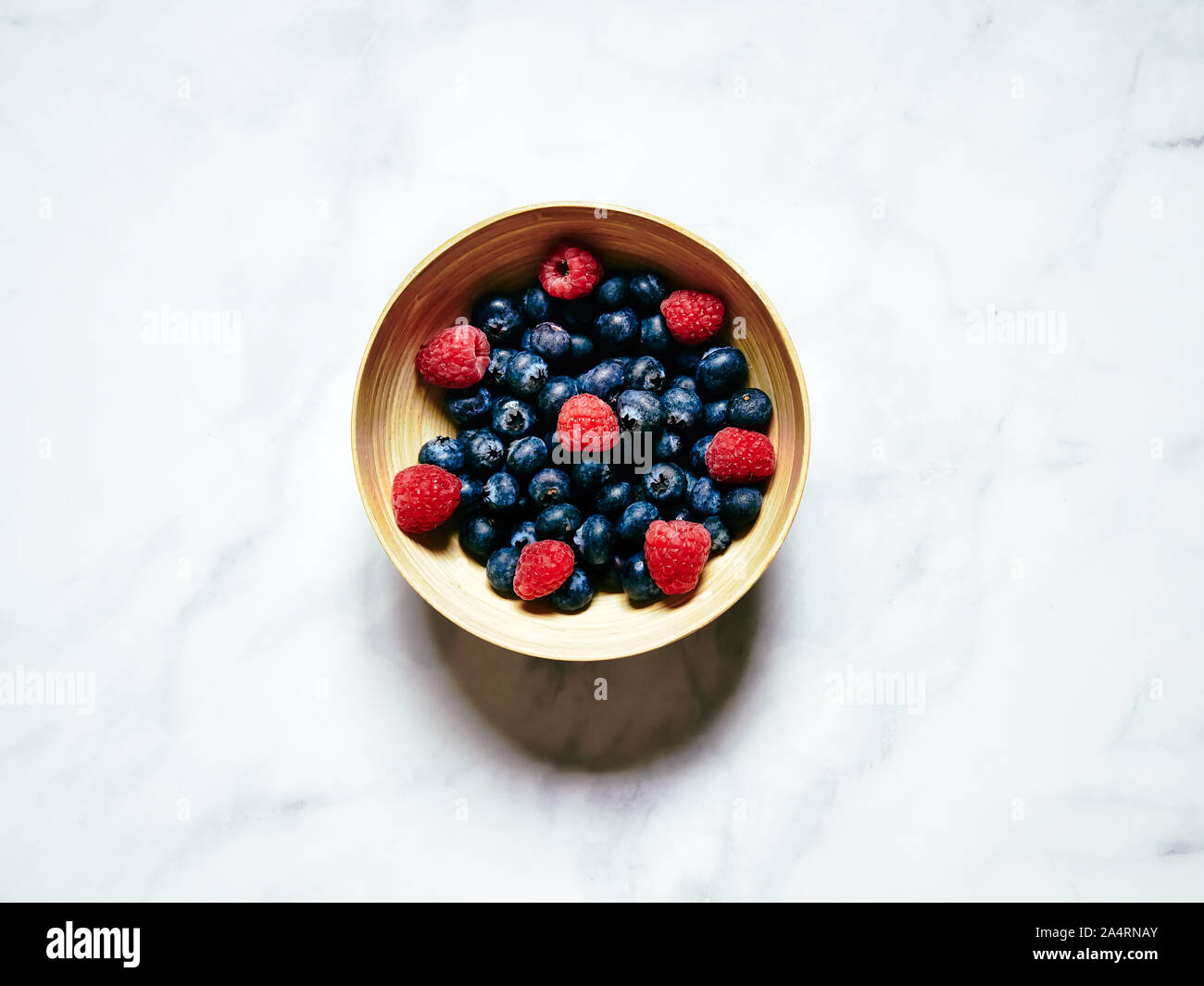 Heidelbeeren und Himbeeren in einer Creme Teller auf einem weißen Marmor Hintergrund betrachtet von oben, flatlay Konzept im Studio Stockfoto