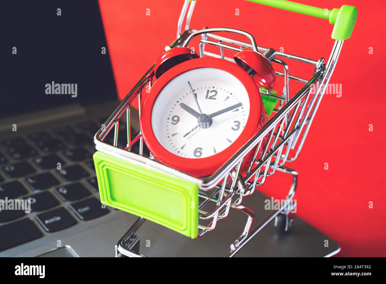 Warenkorb und Wecker auf Laptop auf rotem Hintergrund, Ansicht schließen Stockfoto