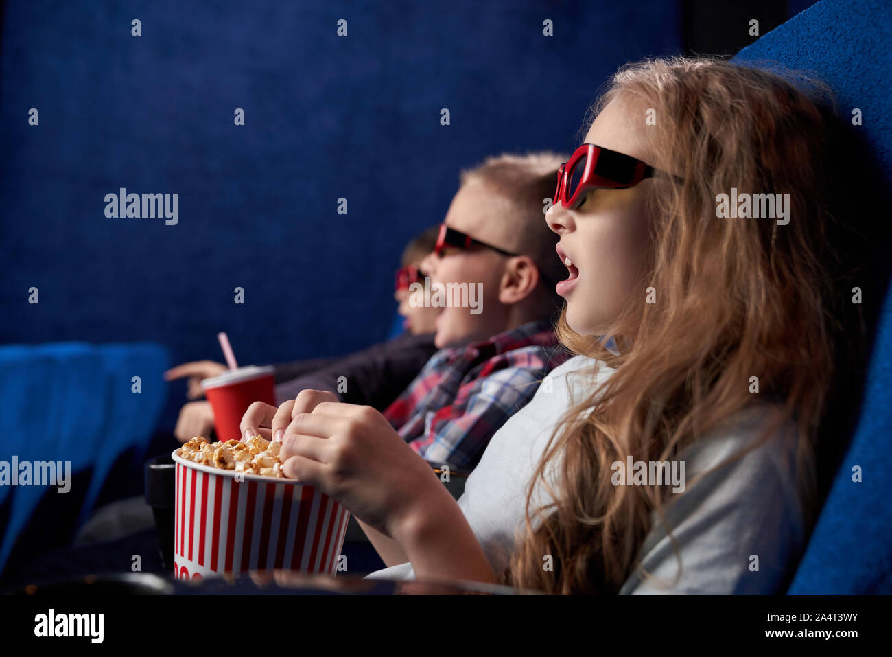Mädchen mit geöffneten Augen beobachten erstaunlicher Film in Film House schockiert. Aufgeregte Kinder tragen 3D-Brille sitzen zusammen, Essen lecker Popcorn im Cine Stockfoto