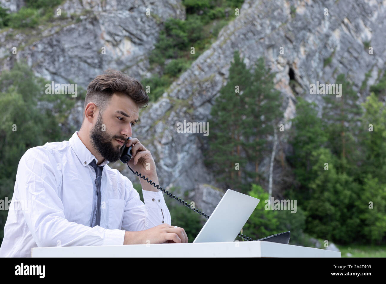 Arbeitnehmer Mann an Schreibtisch mit Computer Laptop und Telefon am Arbeitsplatz, an Bildschirm schaut. Outdoor junge Hipster in Gespräch am Telefon Stockfoto
