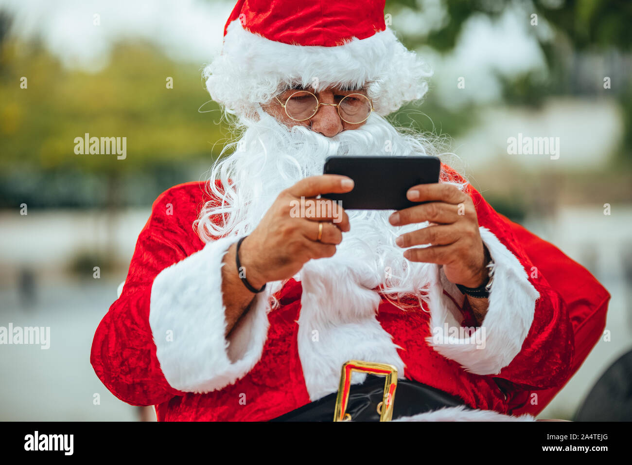Foto von Santa Claus in einem Gespräch mit einem Mobiltelefon mit einem Park hinter unfocused. Weihnachten Stockfoto