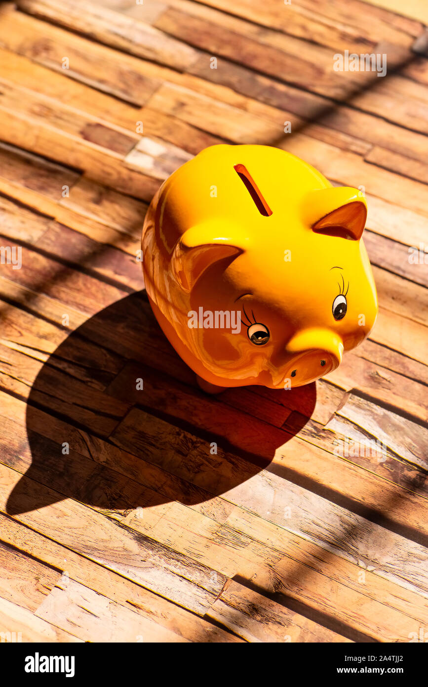 Eine gelbe Sparschwein steht auf einem Holzboden und wirft einen starken Schatten Stockfoto