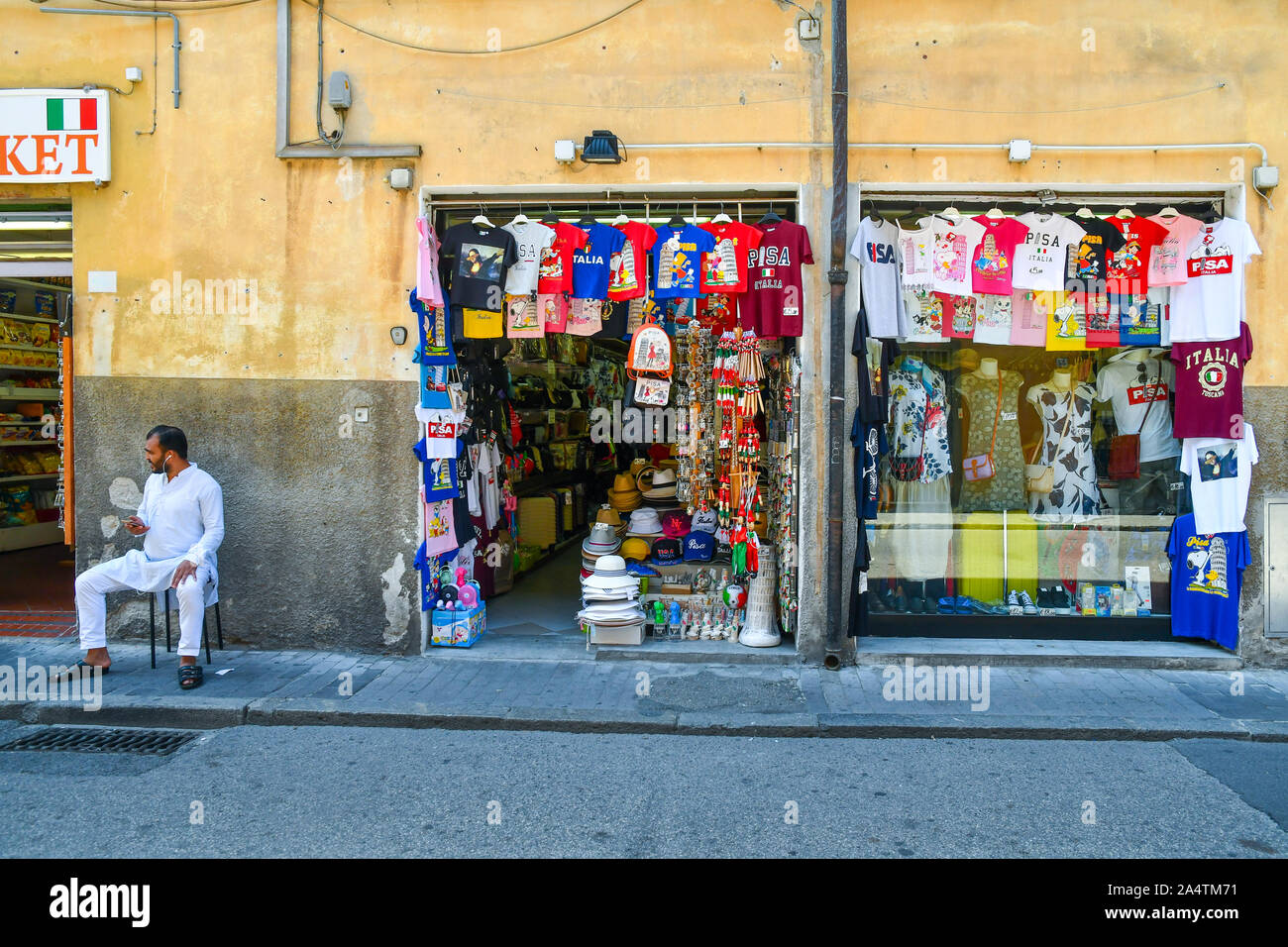Blick auf die Straße mit einem ausländischen Ladenbesitzer vor seinem Souvenirshop im historischen Zentrum der berühmten Stadt Pisa, Toskana, Italien sitzen Stockfoto