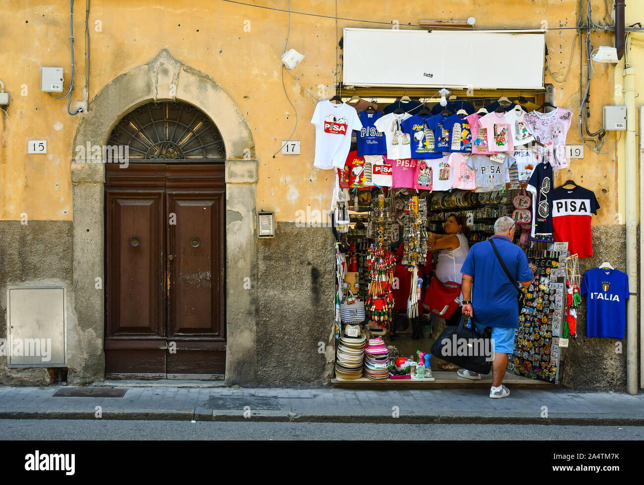 Street View mit Touristen Einkaufen in einem Souvenirshop neben einem alten Eingangstür im historischen Zentrum der berühmten Stadt Pisa, Toskana, Italien Stockfoto