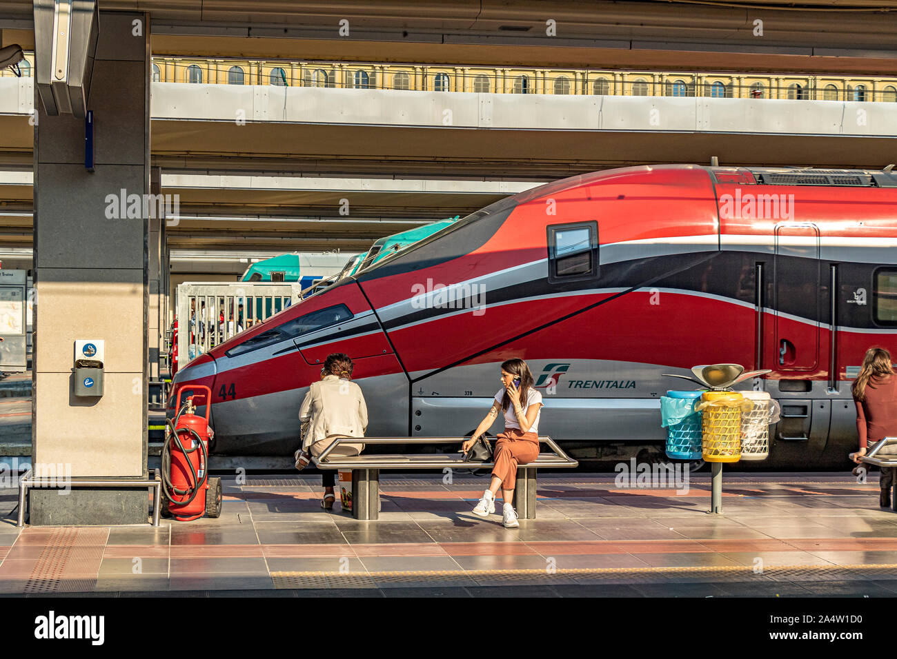 Ein Mädchen sitzen auf einer Bank im Gespräch über ihr Mobiltelefon vor einem Trenitalia Weingut Frecciarossa 1000 High Speed Zug am Bahnhof Porta Nuova, Turin Stockfoto