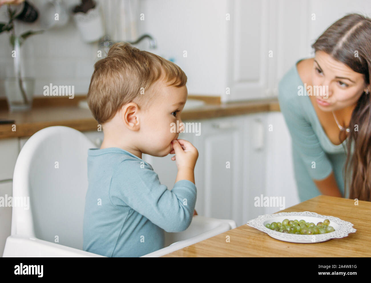 Charmante konzentriert baby boy Essen zunächst Essen Grüne Traube auf die helle Küche zu Hause Stockfoto