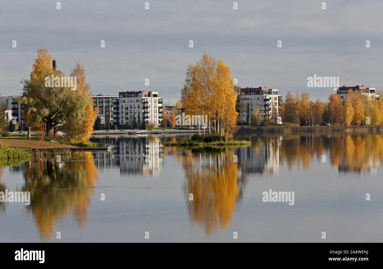 Ein herbstlicher Blick auf die Stadt mit gelben Birken und ruhigen See Oberfläche mit Reflexionen Stockfoto
