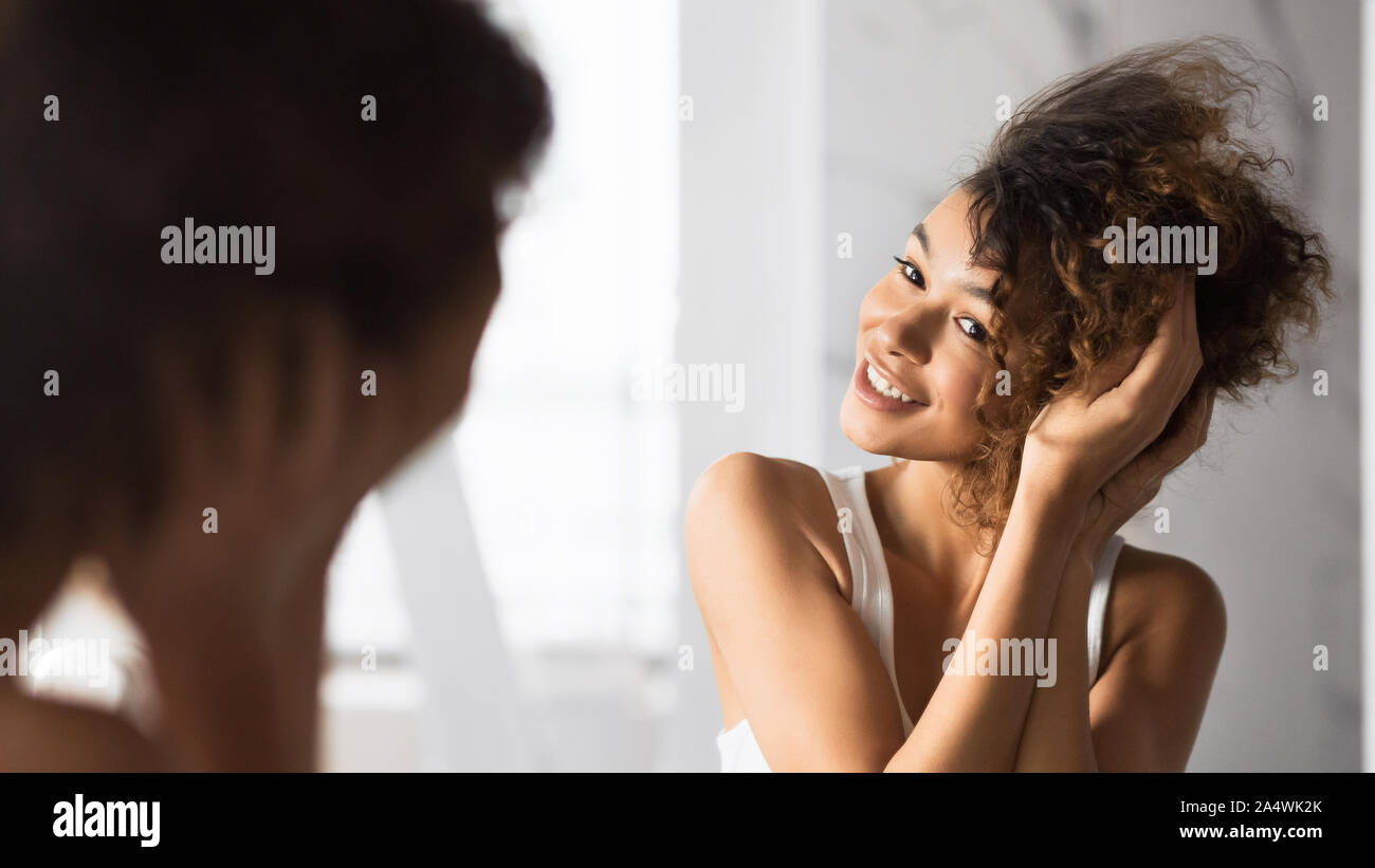 Schwarze Mädchen berühren Haar lächelnd Stand im Badezimmer, Panorama Stockfoto