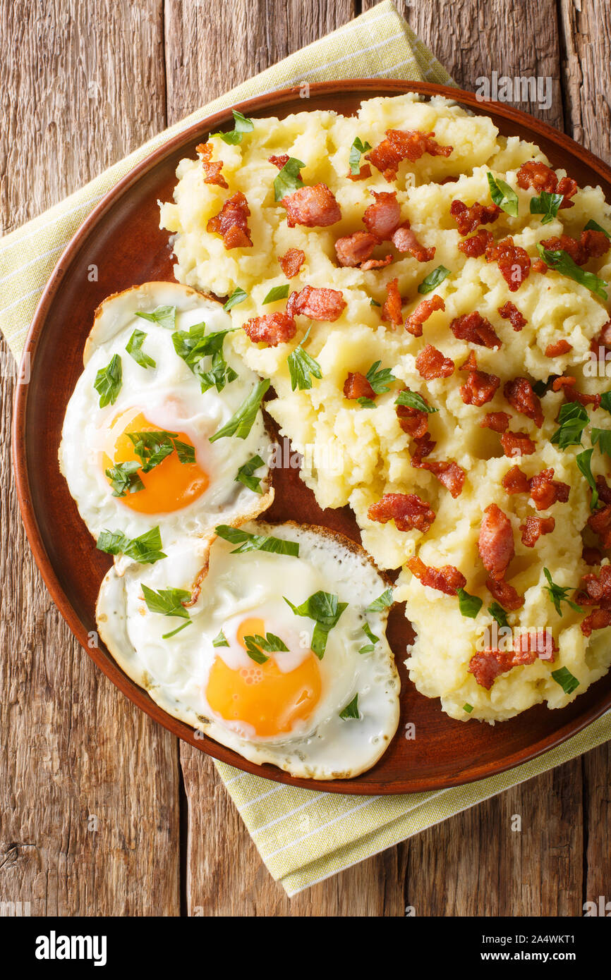 Gewürztem Kartoffelpüree mit Speck und Petersilie mit Spiegelei in der Nähe serviert auf einem Teller auf den Tisch. Vertikal oben Ansicht von oben Stockfoto