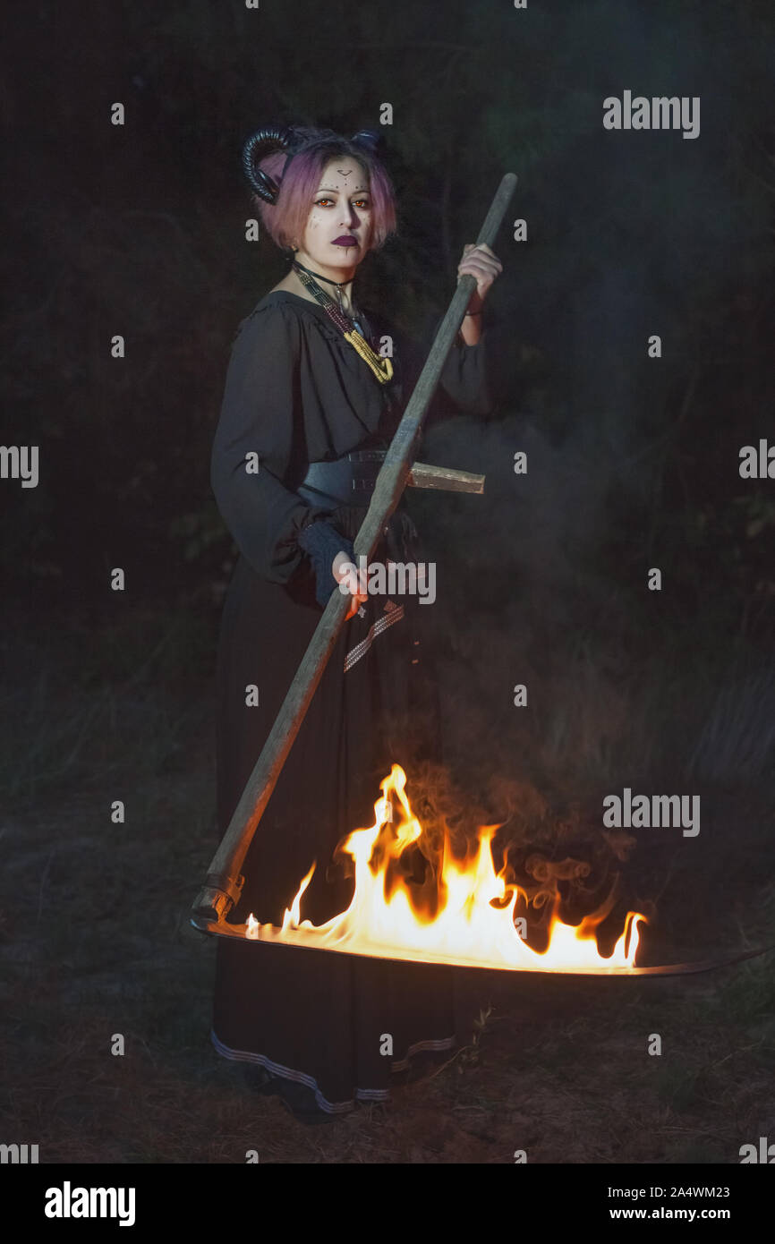 Weibliche Grim Reaper, den Rasen mäht und in der Dunkelheit mit einem brennenden Sense. Stockfoto