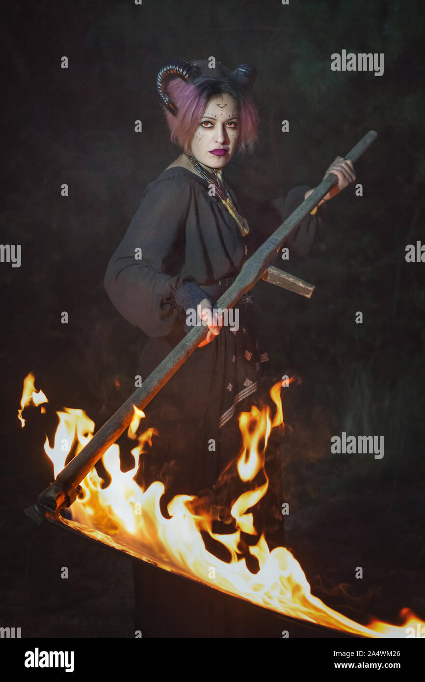 Düstere weiblicher Dämon, den Rasen mäht und in der Dunkelheit mit einem brennenden Sense. Stockfoto