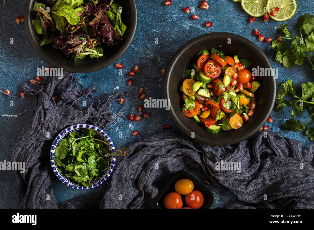 Frischer Salat mit Tomaten, Gurken und Kräuter, flach über dem Salat ist in einem schwarzen Schüssel, und es gibt andere Schüsseln mit Zutaten um ihn herum. T Stockfoto