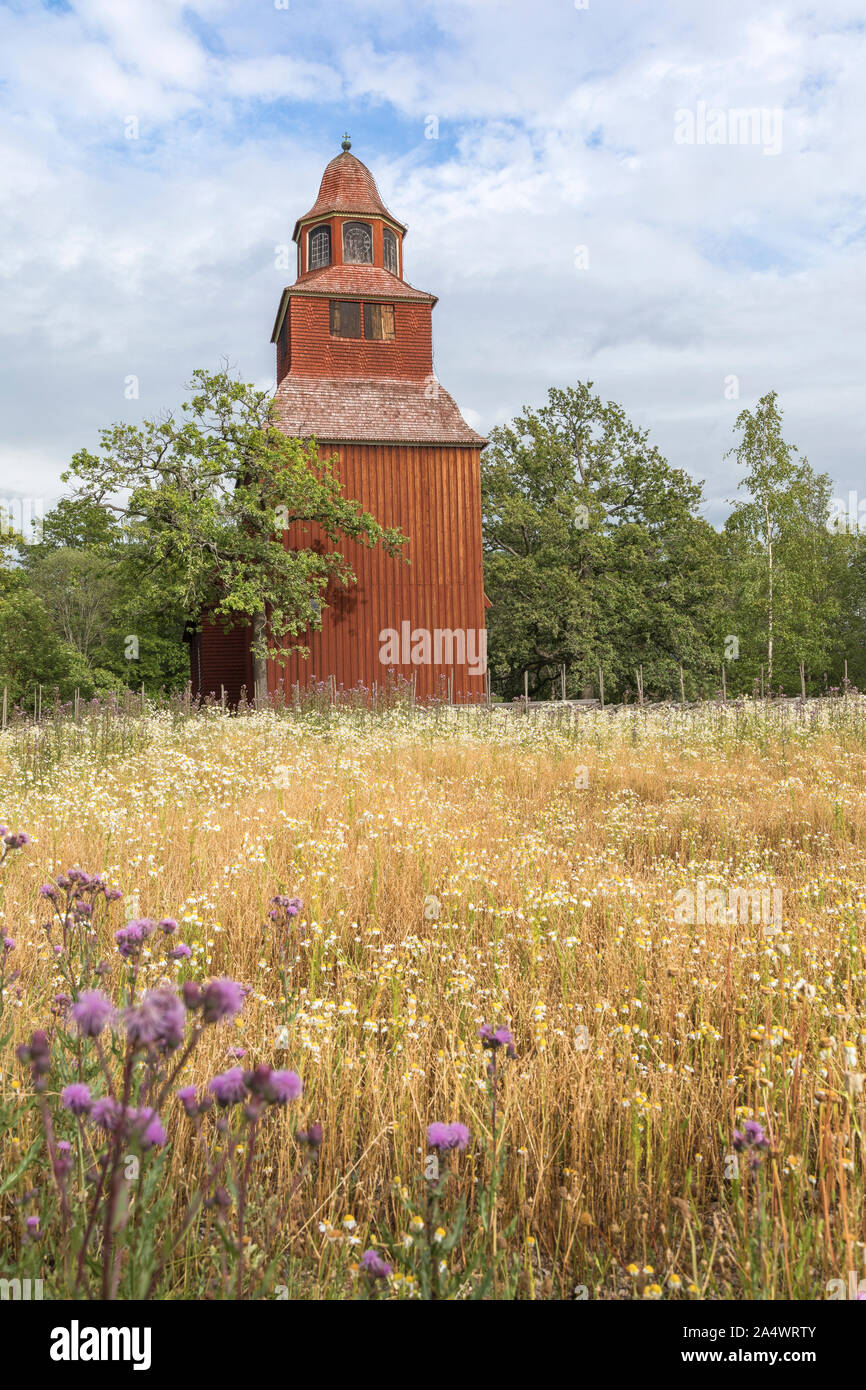Schwedische Landschaft Landschaft mit einer alten Holzkirche. Die hölzerne Kirche in traditionellen schwedischen Falu rote Farbe gestrichen und es ist trocken Gras und Fl Stockfoto