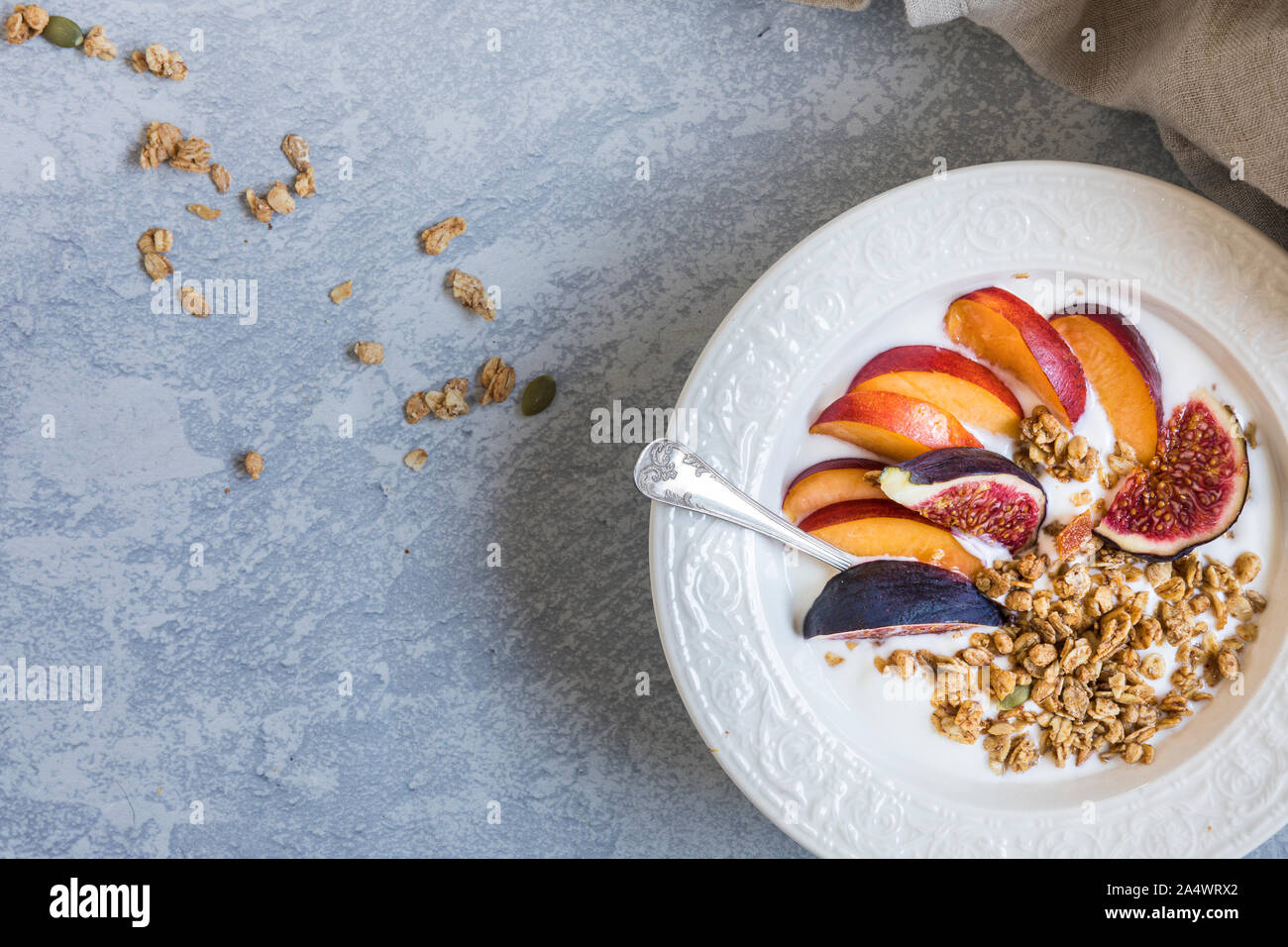 Close-up ein eine weiße Schale mit Müsli Müsli mit frischem Obst, Feigen und Nektarinen. Von oben, flach gesehen. Es ist ein Leinen Servietten neben der Stockfoto
