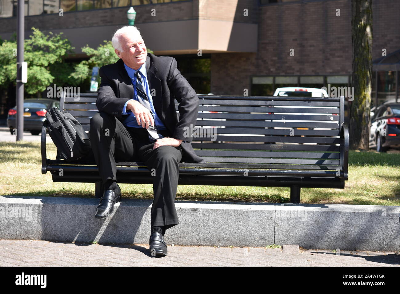 Nach Senior Business Mann lächelnd tragen Anzug sitzt auf der Bank Stockfoto