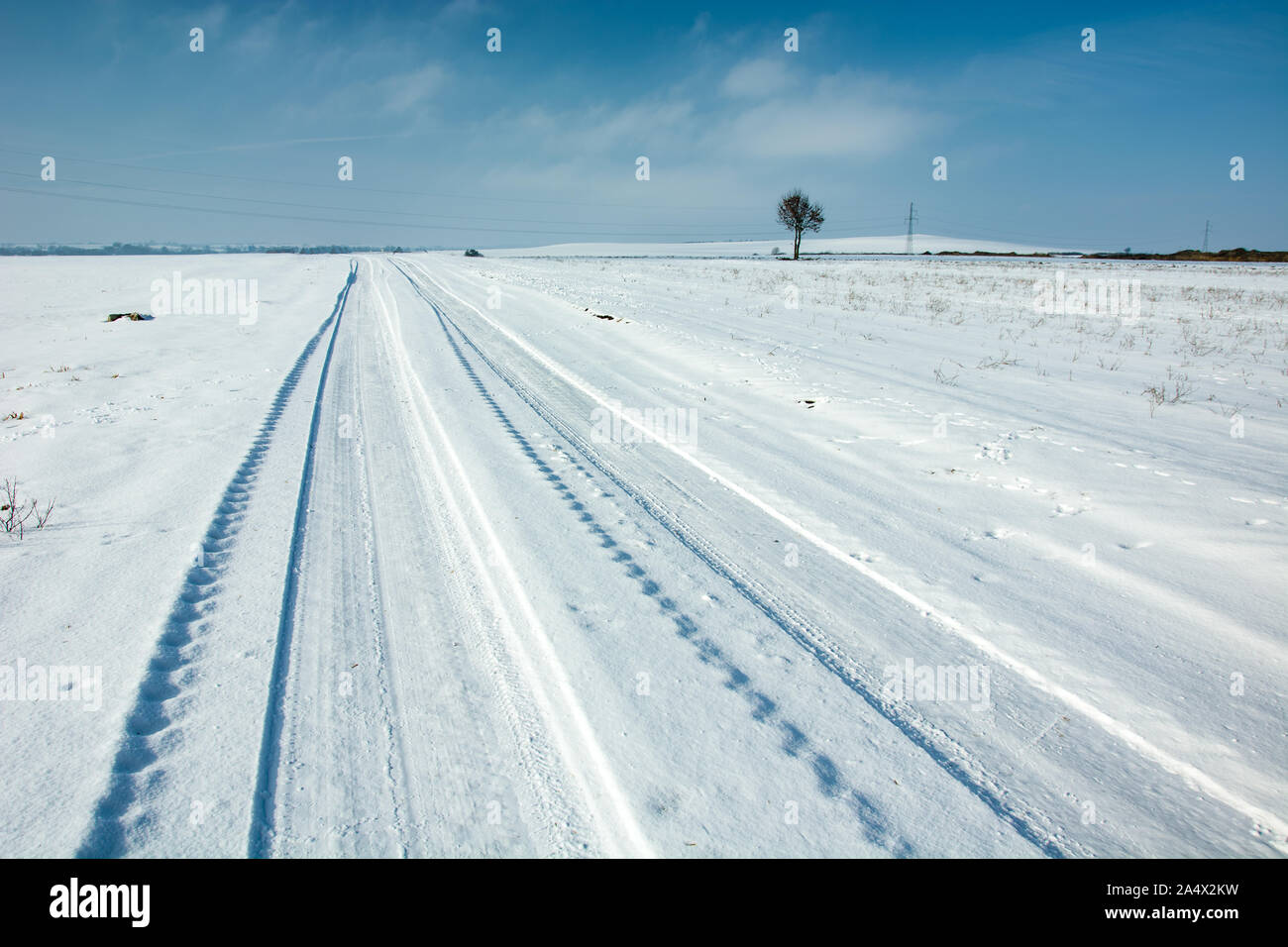 Strasse mit Schnee bedeckt, Radspuren, Horizon und blauer Himmel Stockfoto