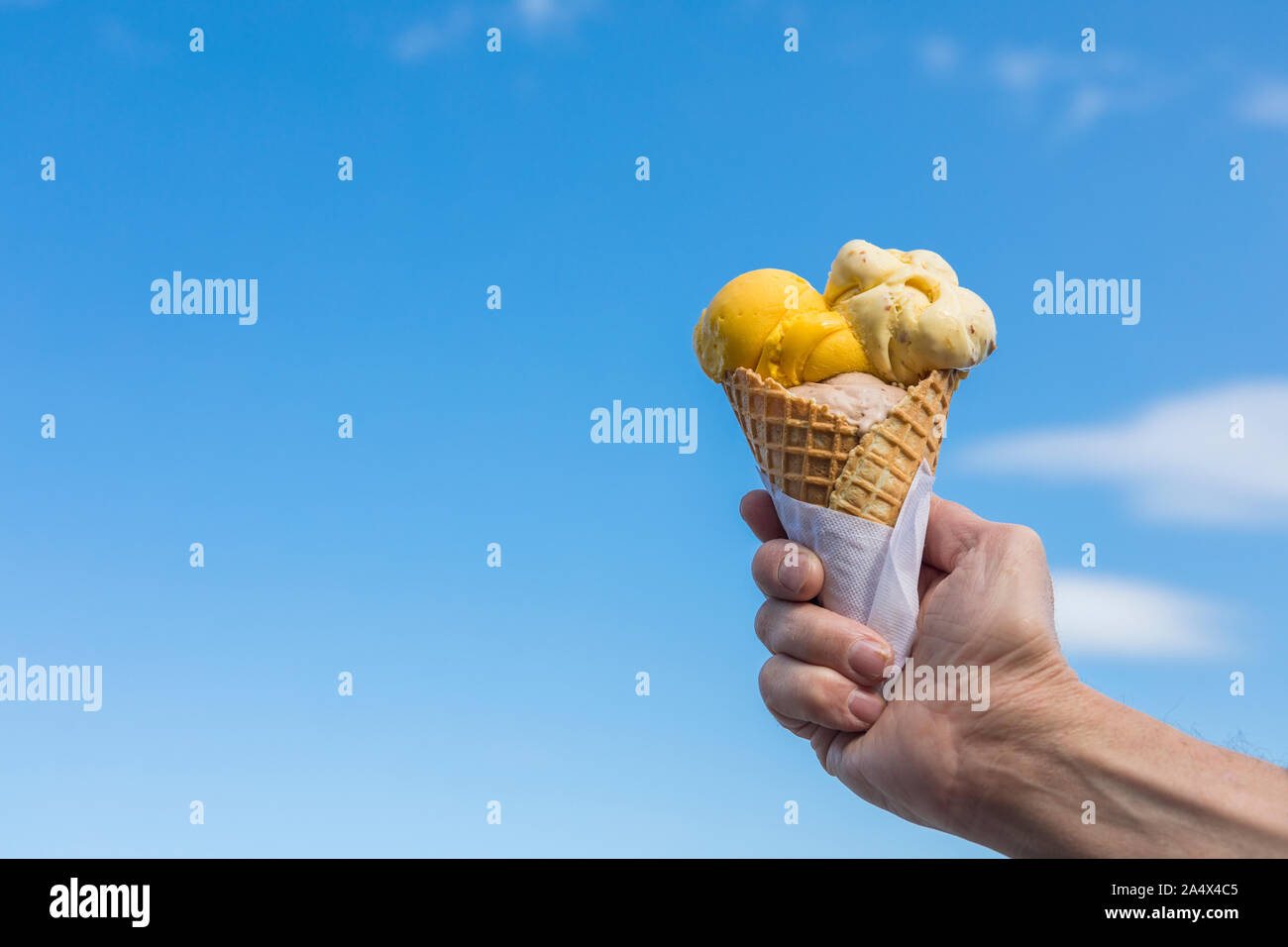 Ein Eis Waffel Kegel mit einem blauen Himmel im Hintergrund. Gelb, beige und braun gelato Eis in ein Eis Waffel Kegel, mit einem blauen Himmel im Hintergrund. Stockfoto